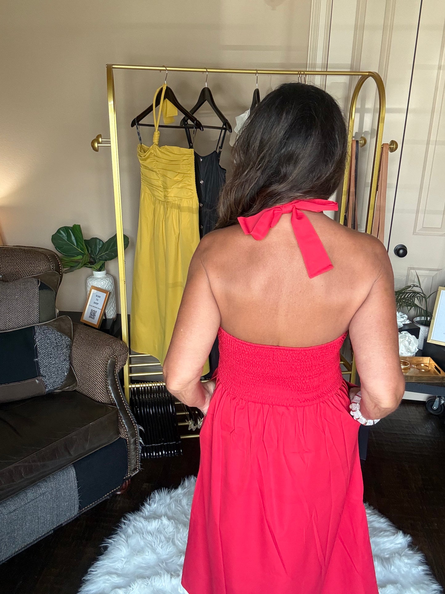 Woman in a red dress standing in front of a clothing rack with yellow and black dresses.
