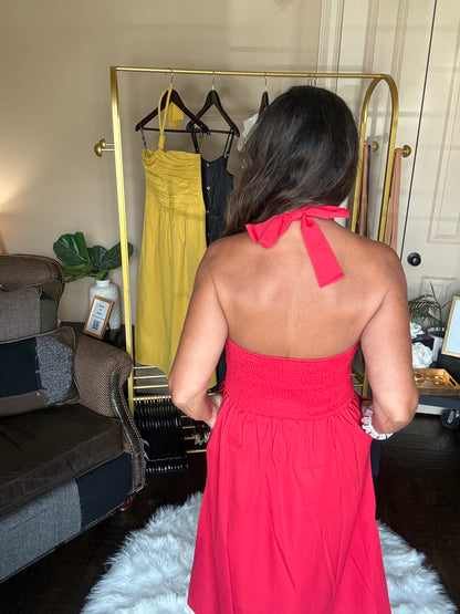 Woman in a red dress standing in front of a clothing rack with yellow and black dresses.