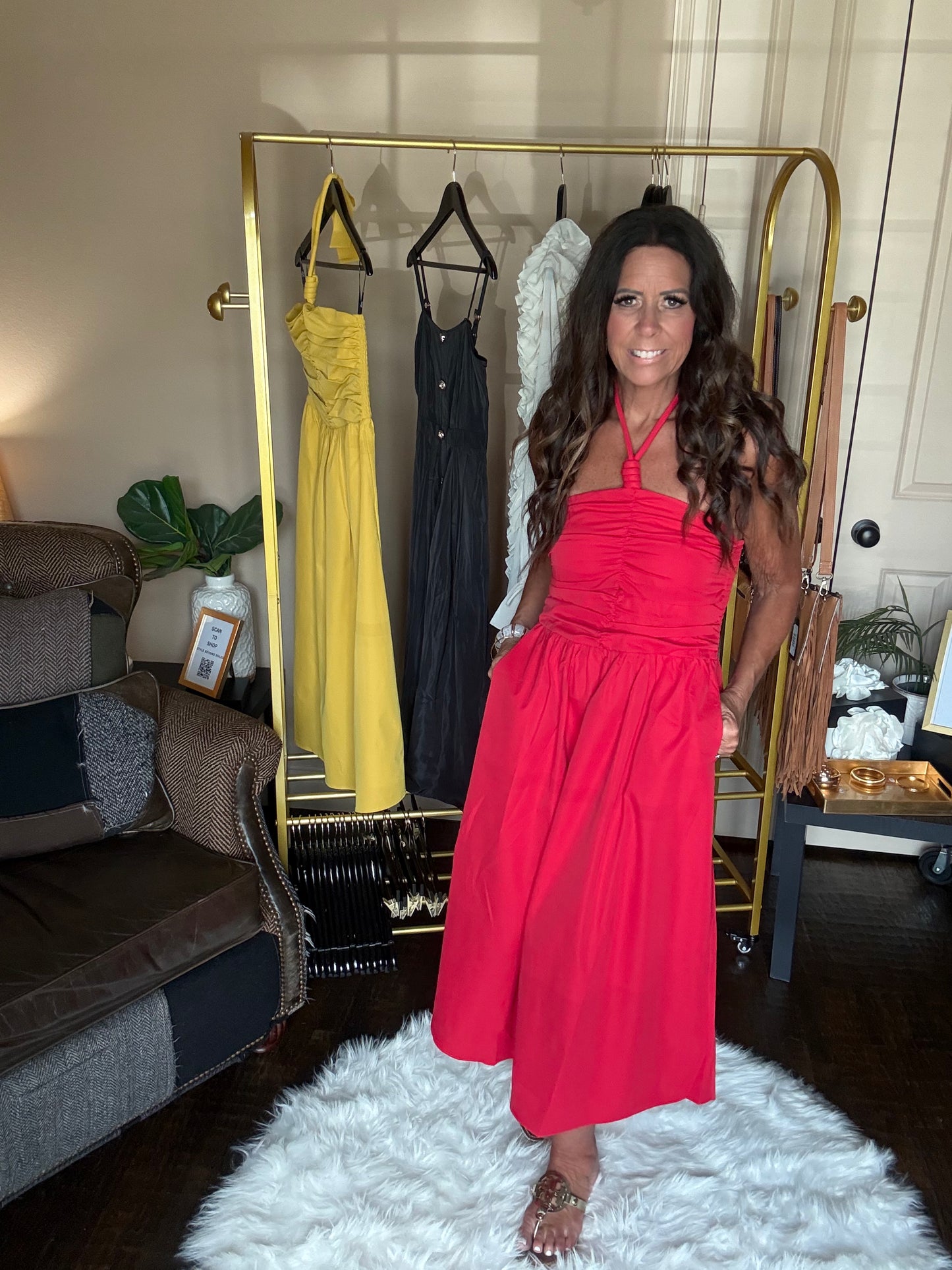 Woman in a red dress standing in front of a rack with other dresses in a room.