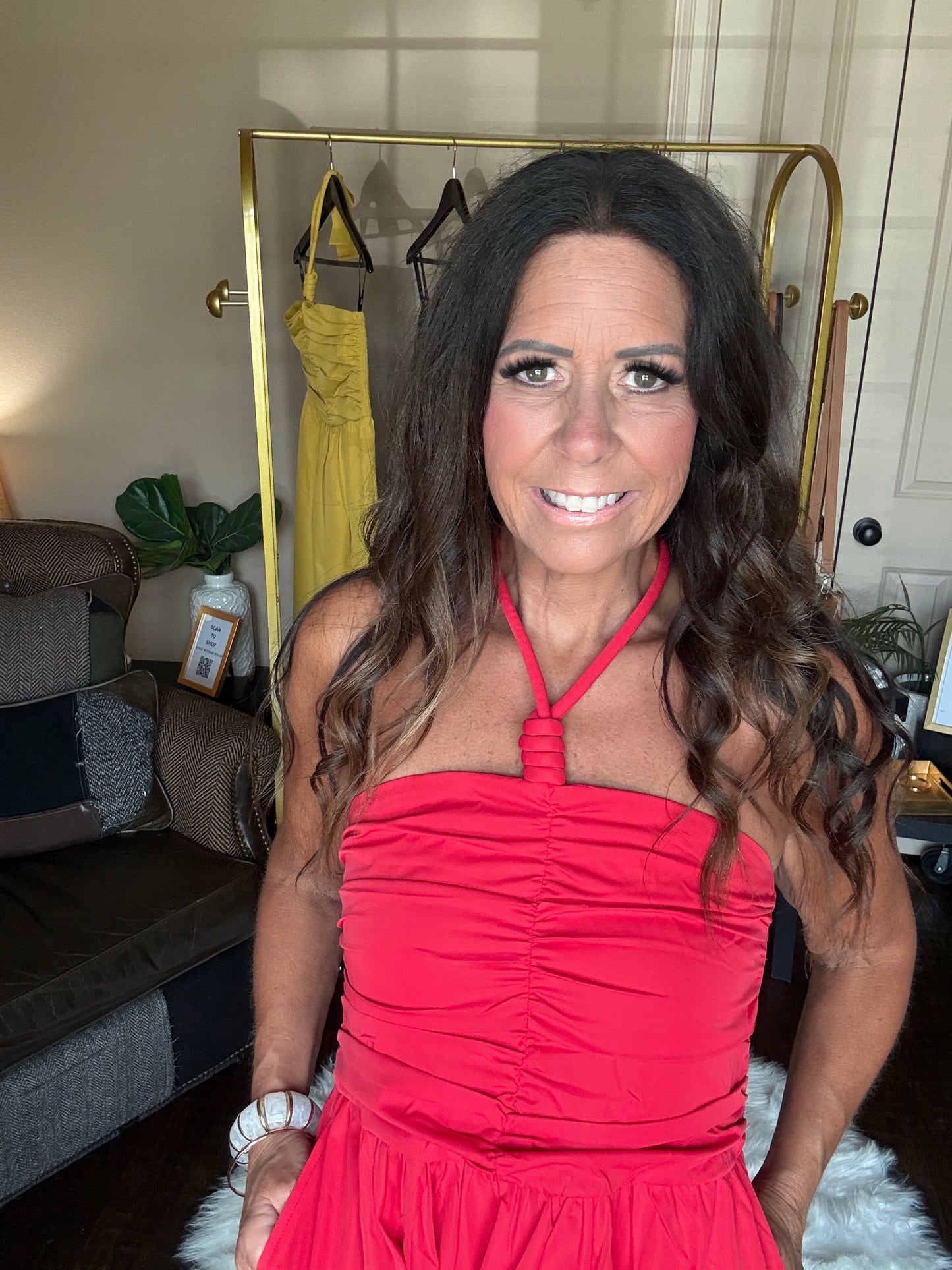 Woman wearing a red dress in a room with a gold rack and yellow dress in the background.