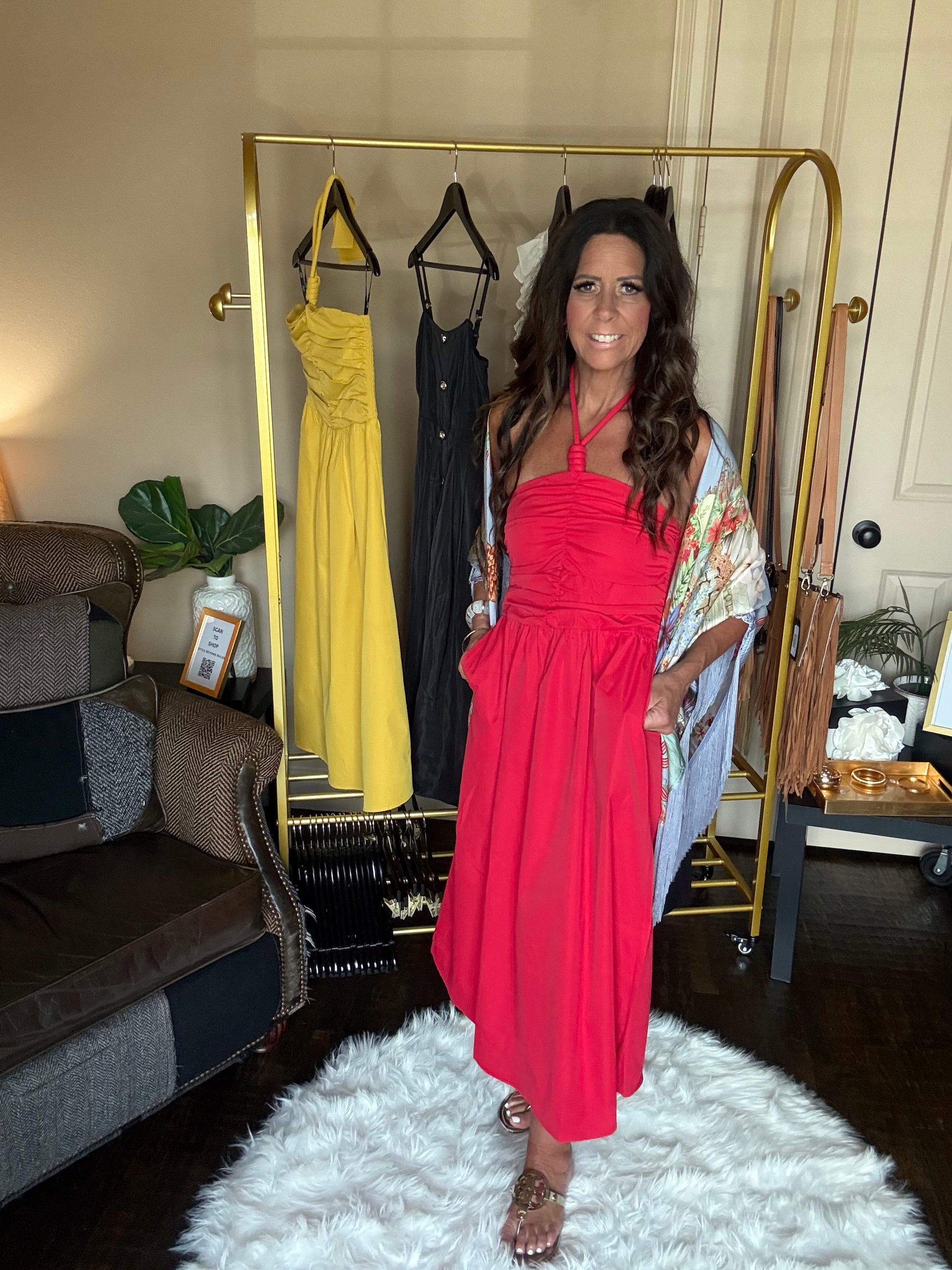 Woman in a red dress standing in a room with a rack of dresses and a chair.
