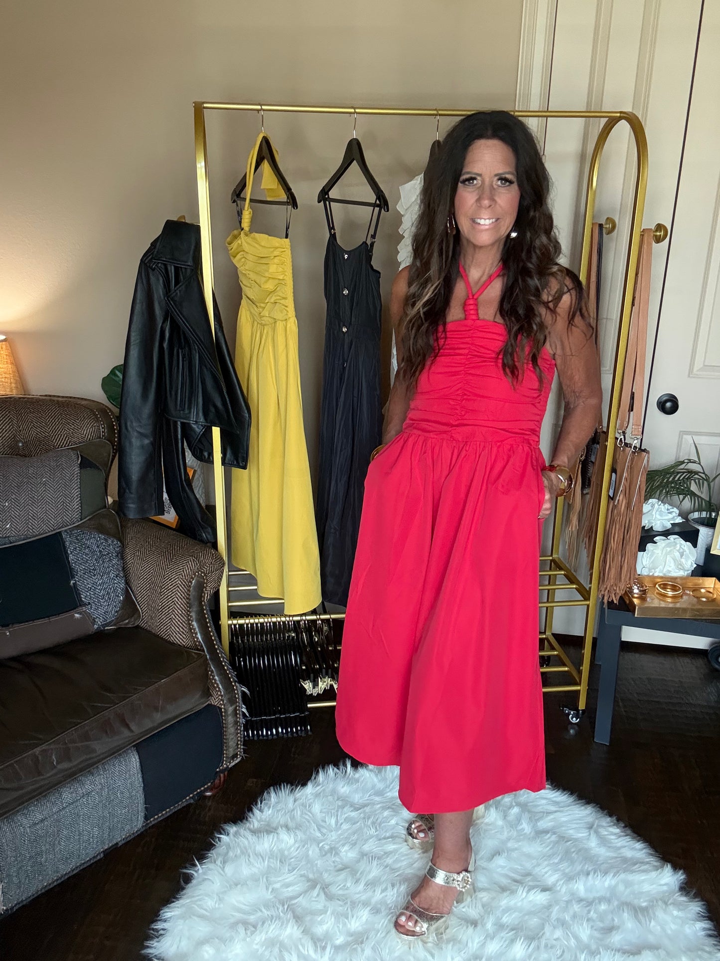 Woman in a red dress standing in a room with a rack of dresses and a couch.