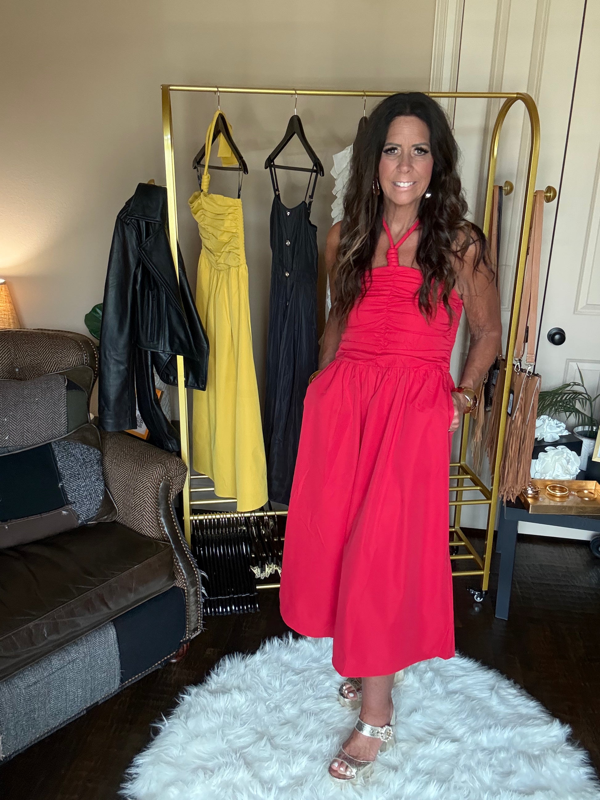 Woman in a red dress standing in a room with a rack of dresses and a couch.