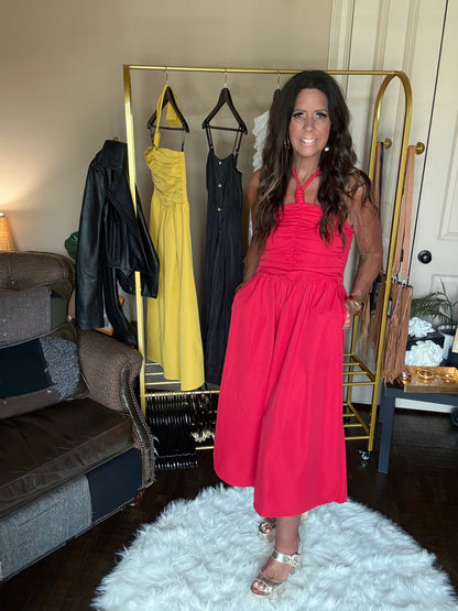 Woman in a red dress standing in a room with a rack of dresses and a couch.