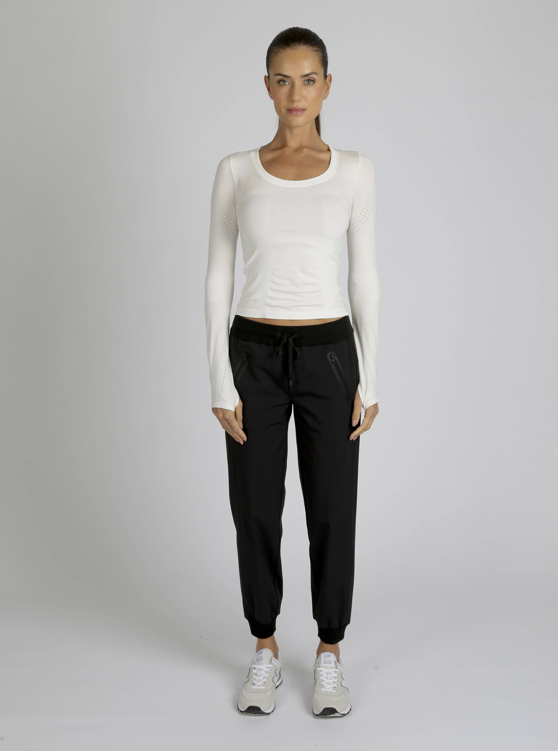 Woman wearing a white long-sleeve top and black pants on a gray background