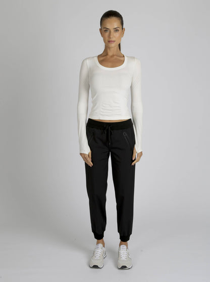 Woman wearing a white long-sleeve top and black pants on a gray background