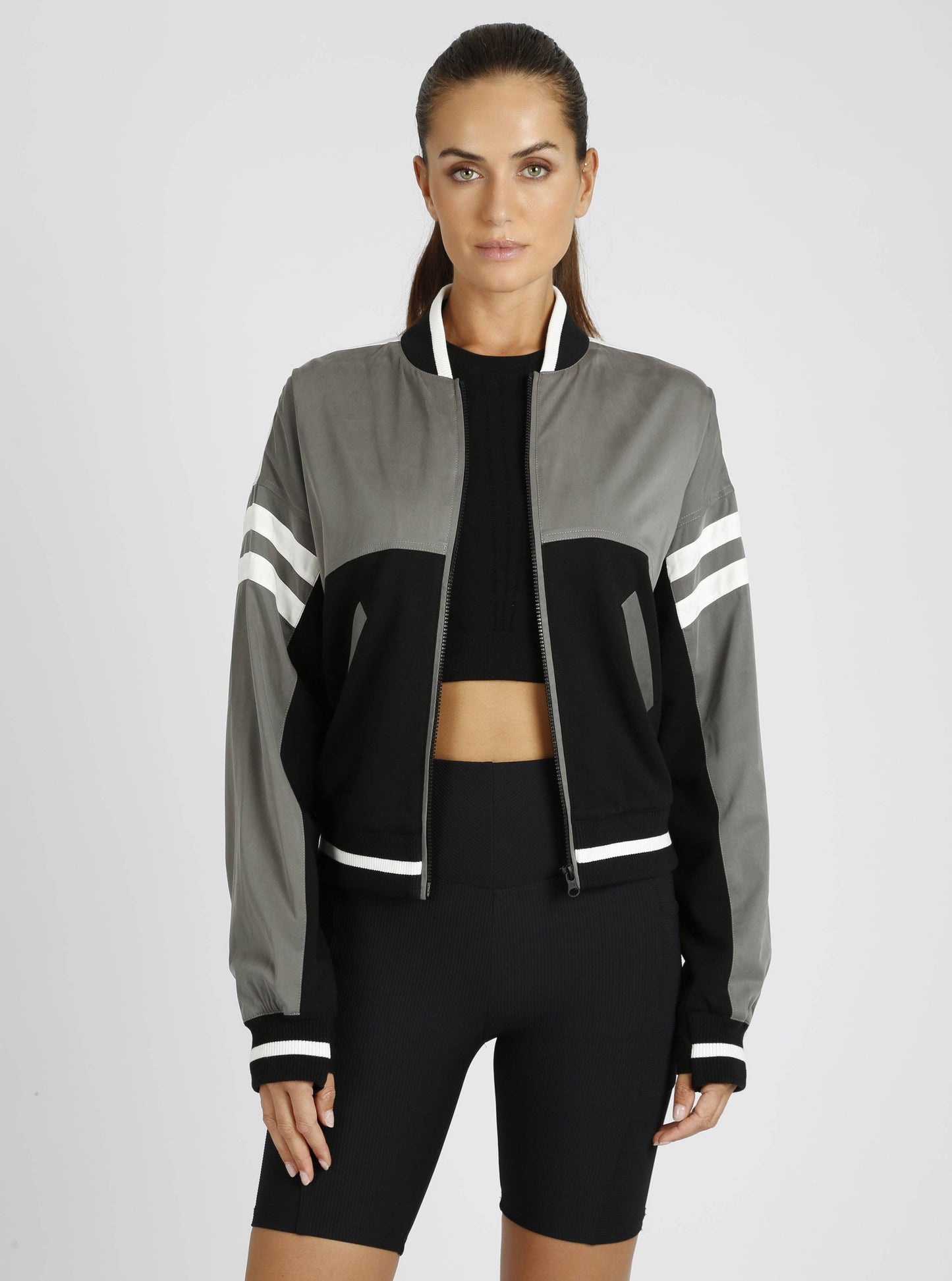 Woman wearing a gray and black jacket with white stripes on a light gray background