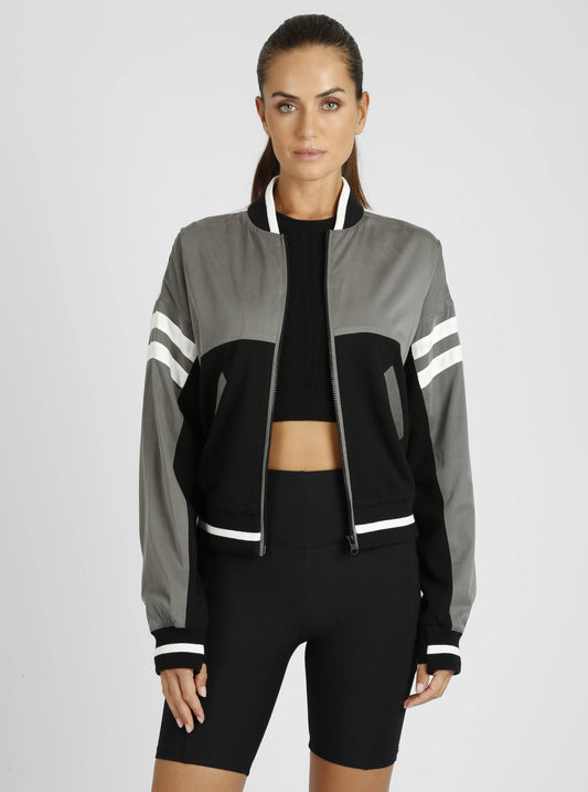 Woman wearing a gray and black jacket with white stripes on a light gray background
