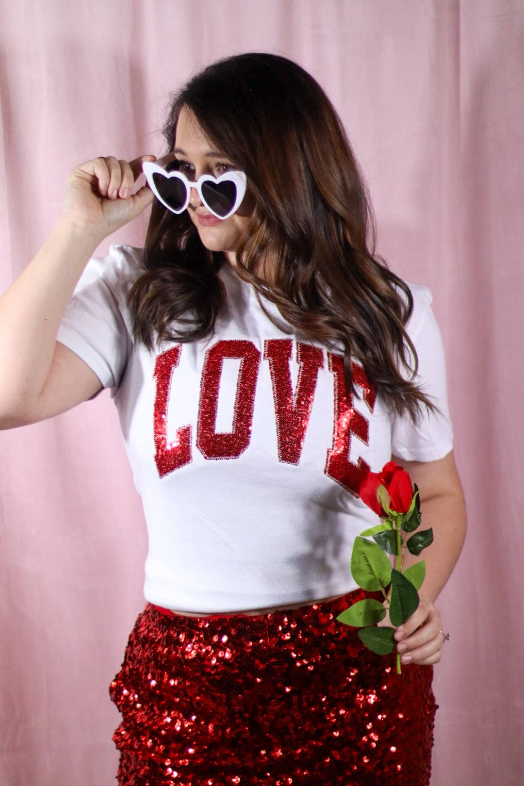 Woman wearing a 'LOVE' shirt and red sequin skirt with a pink background