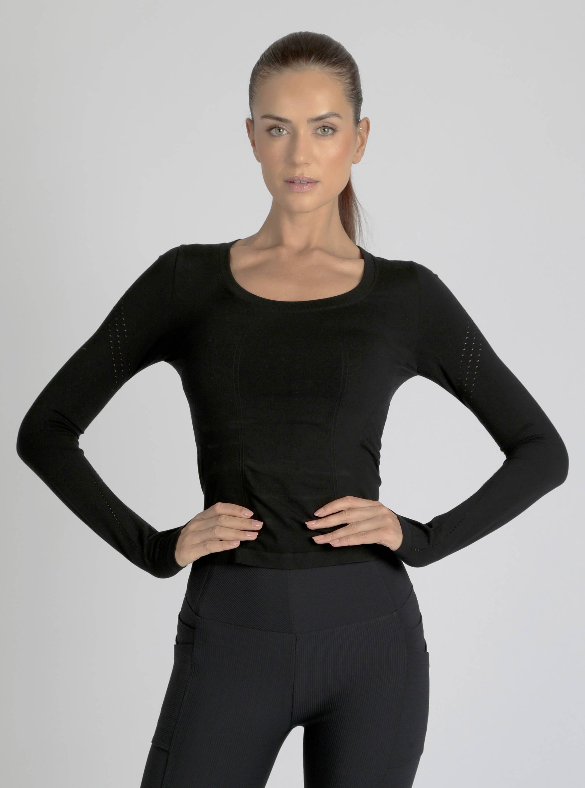 Woman wearing a black long-sleeve top and black leggings against a gray background