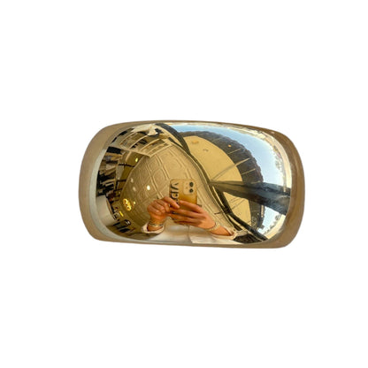 Gold-colored car mirror reflecting a person holding a phone.