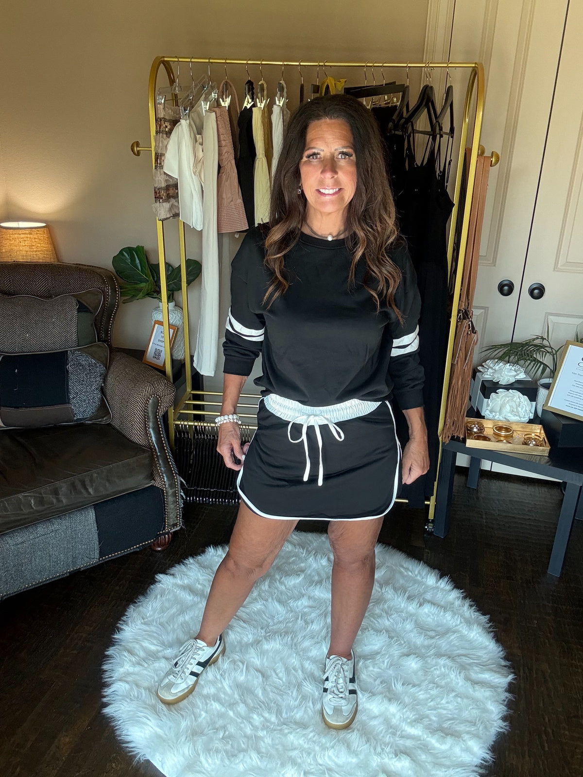 Woman in black and white outfit standing on a white rug in a room with a clothing rack.