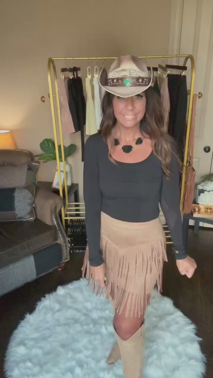 Woman modeling a tan fringe mini skirt in a home boutique.
