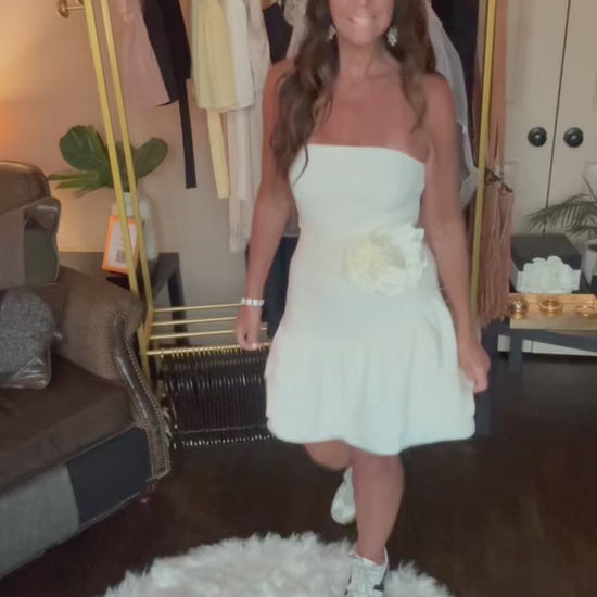 Woman in a white dress standing in a room with a clothing rack and decor.