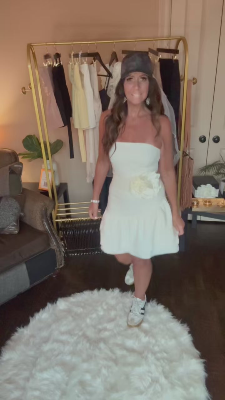 Woman in a white dress standing in a room with a clothing rack and decor.