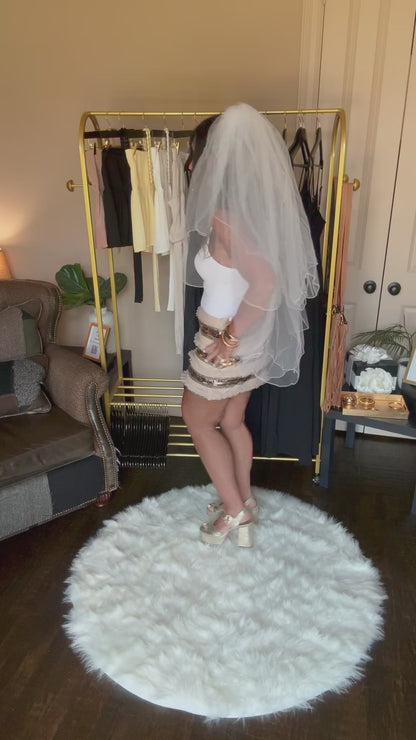 Video of a woman standing on a white rug in a room with clothing racks and furniture.