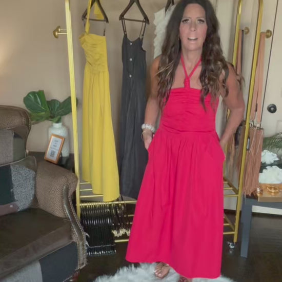 Woman in a red dress standing next to a rack of dresses in a room.