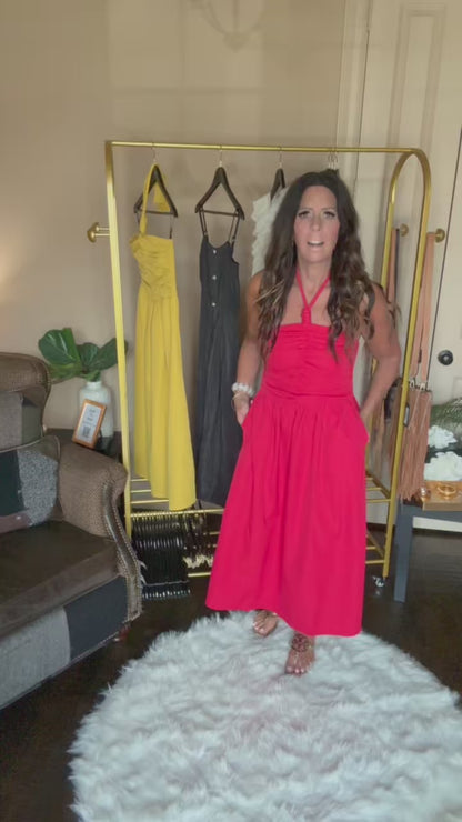 Woman in a red dress standing next to a rack of dresses in a room.
